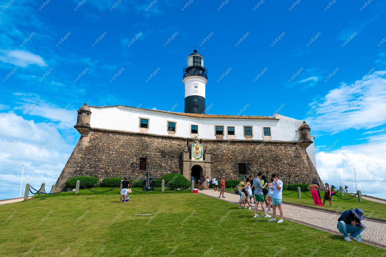 Salvador, Bahia Farol da Barra com arquitetura robusta e pessoas caminhando sob céu azul e vegetação ao redor