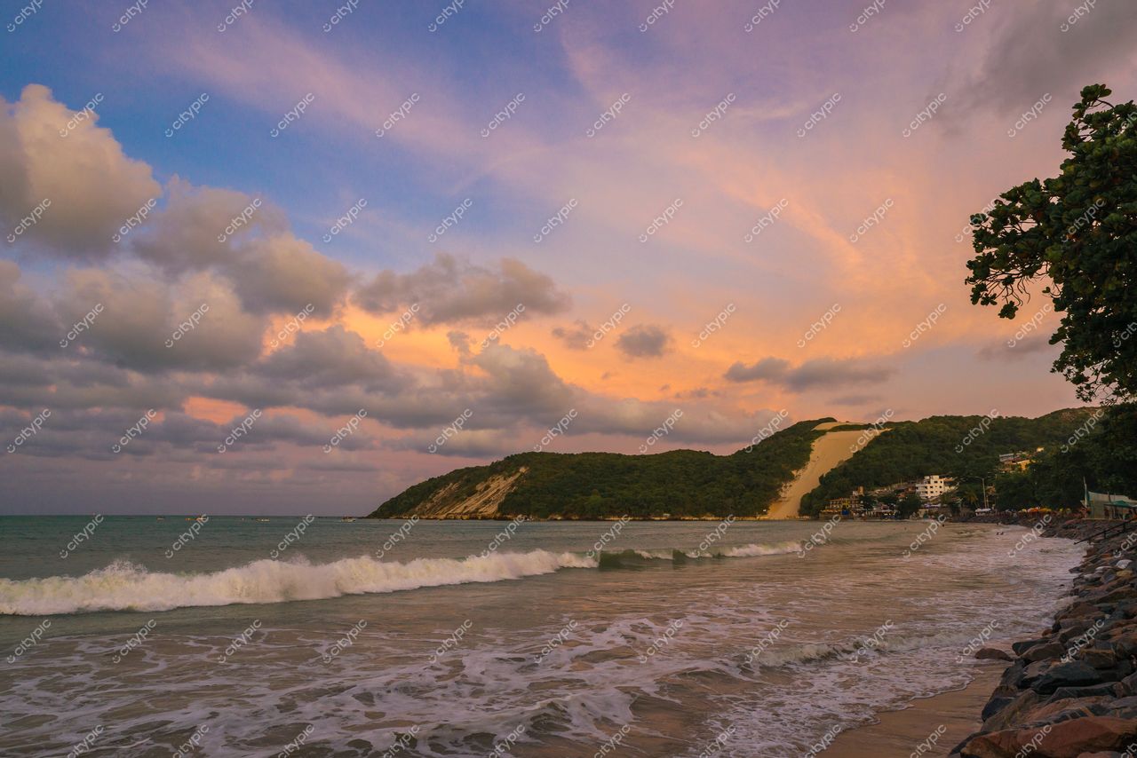 Natal, Rio Grande do Norte, pôr do sol na praia com colina verde e edificações à beira-mar
