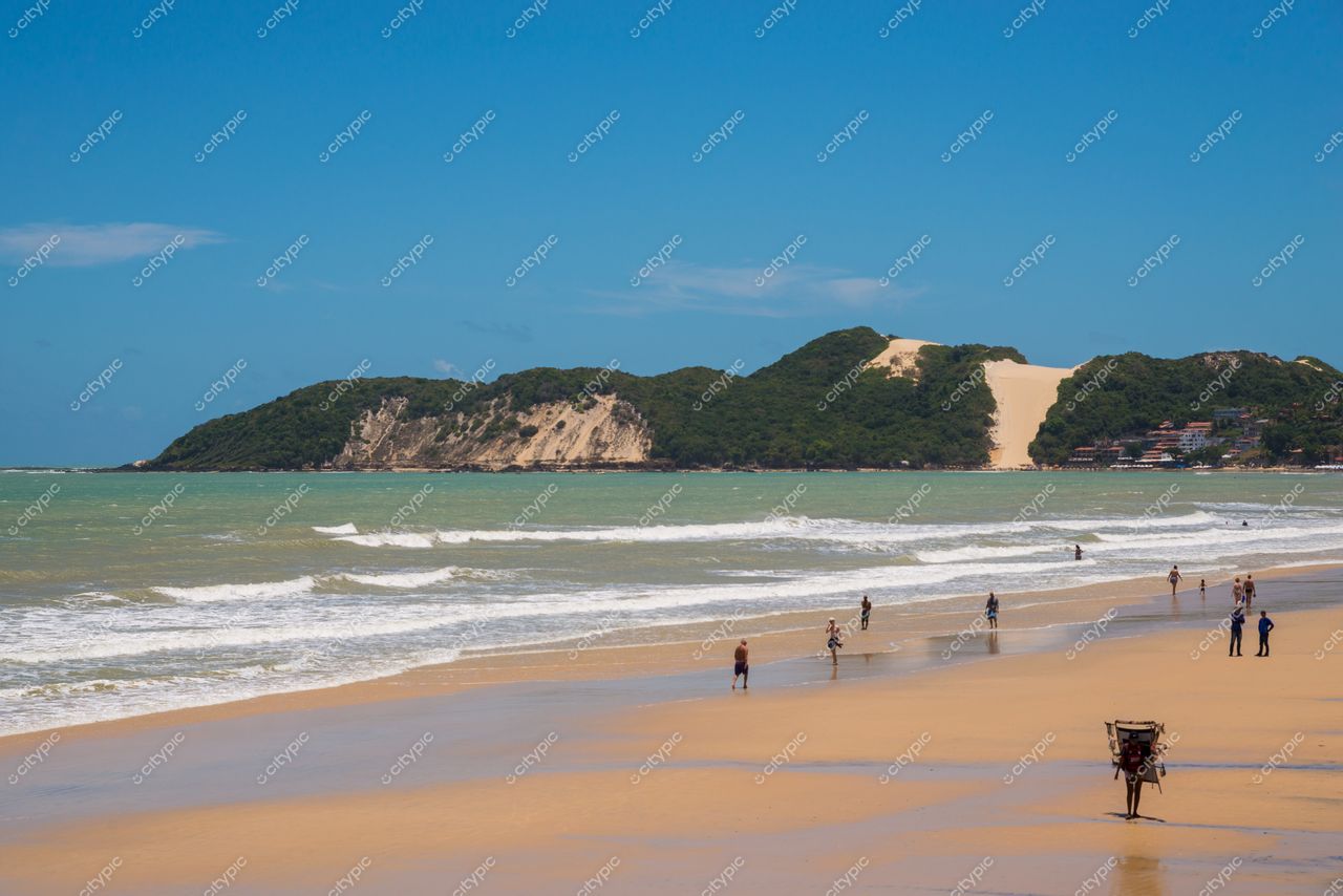 Natal, Rio Grande do Norte com praia tranquila e pessoas caminhando na areia sob céu azul e vegetação densa