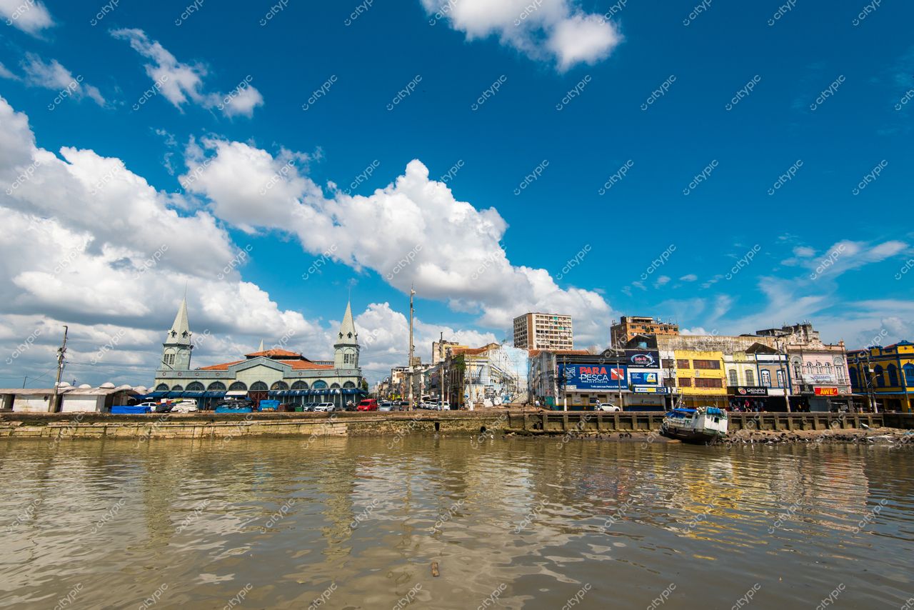 Belém, Pará, cenário urbano à beira do rio com prédios históricos e embarcações ancoradas sob céu azul vibrante