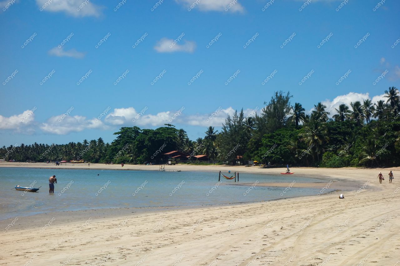 Morro de São Paulo, Bahia, praia tranquila com água calma e rasa, vegetação densa e pessoas caminhando na areia