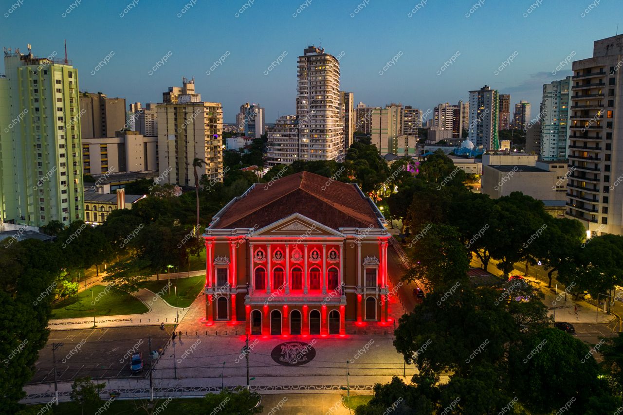 Belém, Pará vista aérea do Theatro da Paz iluminado em vermelho ao entardecer com skyline e áreas verdes ao redor