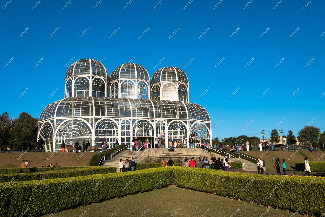 Curitiba, Paraná, Jardim Botânico com estufa de vidro em dia ensolarado e visitantes no gramado ao redor
