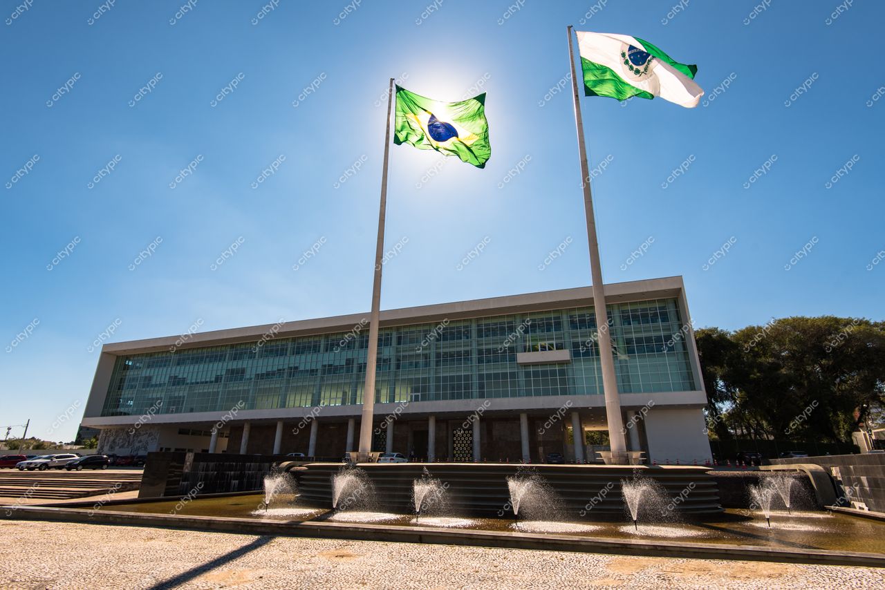 Curitiba, Paraná vista da fachada de edifício moderno com bandeiras ao vento e fontes d’água em dia ensolarado