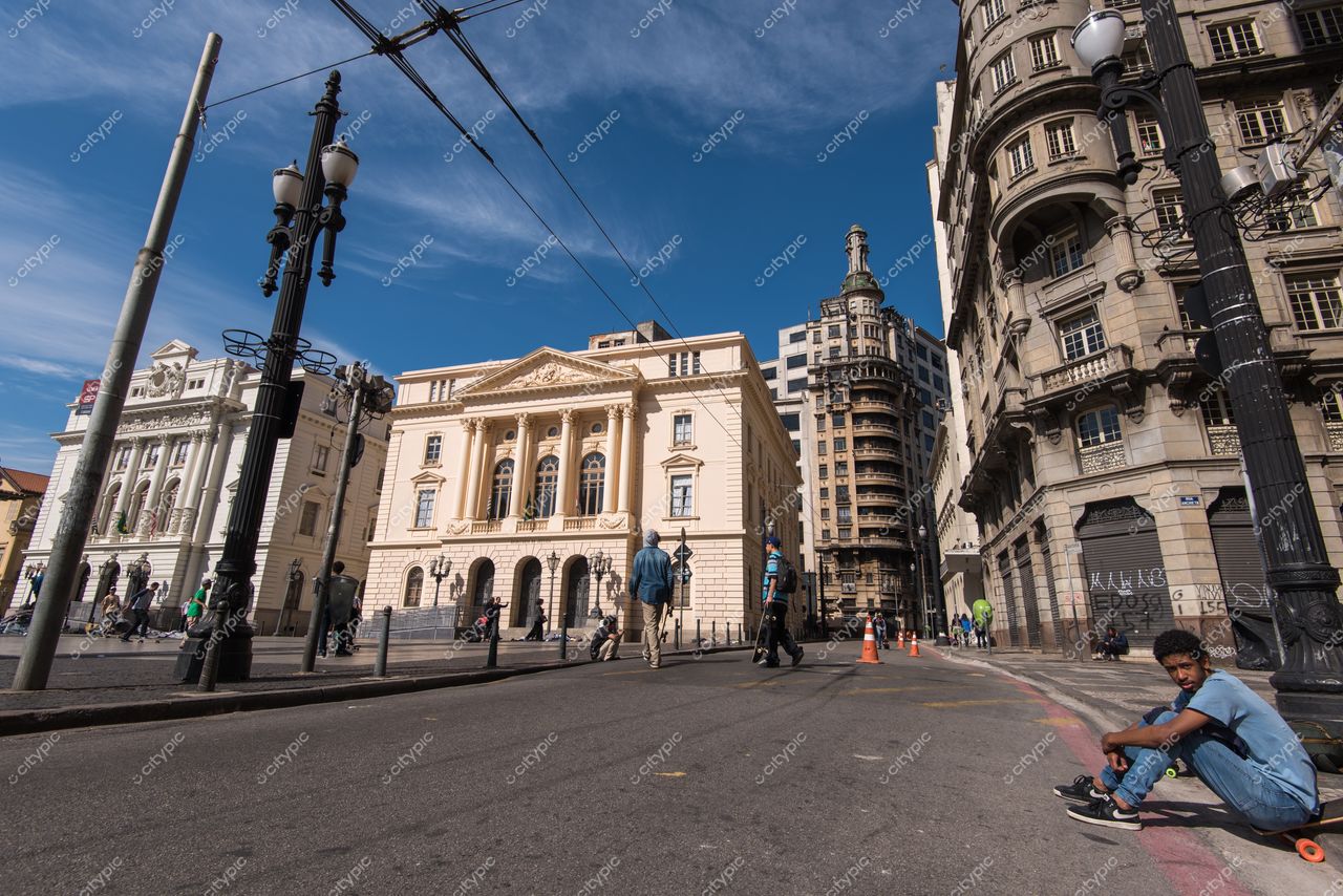 São Paulo, São Paulo, jovem sentado em rua ampla com edifícios neoclássicos e modernos sob luz do dia