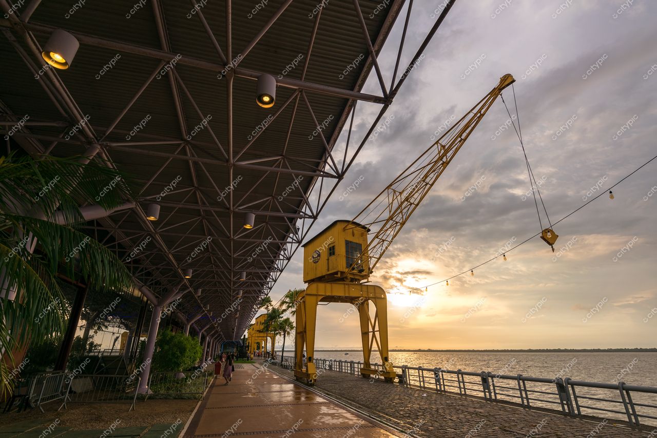 Belém, Pará, guindaste amarelo antigo à beira-mar com calçadão, vegetação e céu nublado ao entardecer