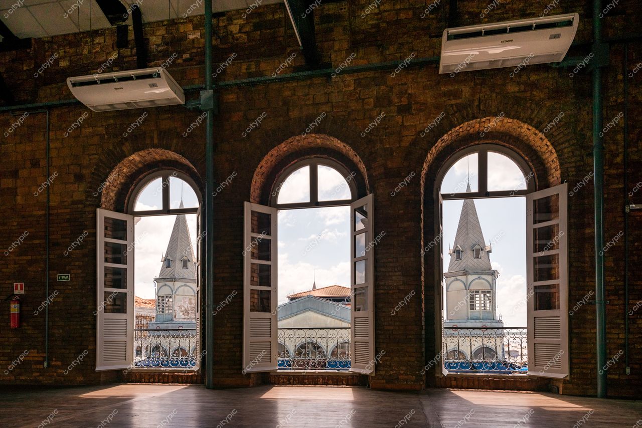 Belém, Pará, janelas de madeira abertas com vista para torres coloniais sob céu claro em ambiente interno