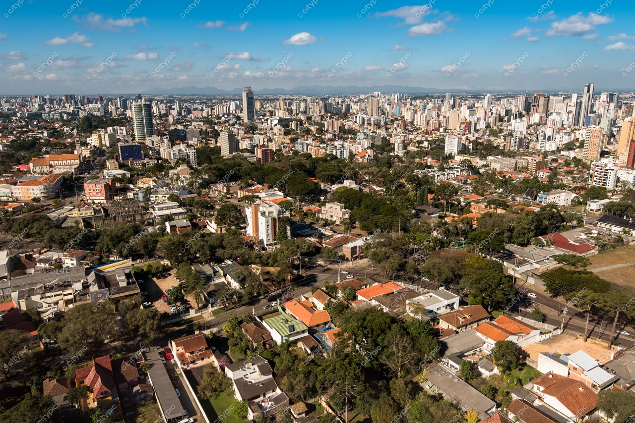 Curitiba, Paraná vista aérea em dia claro com edifícios altos, áreas residenciais e vegetação abundante intercaladas