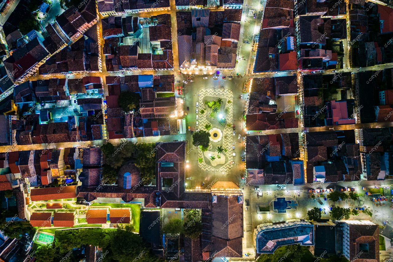 Salvador, Bahia vista aérea ao entardecer com ruas sinuosas, edificações históricas e vegetação ao redor da praça iluminada