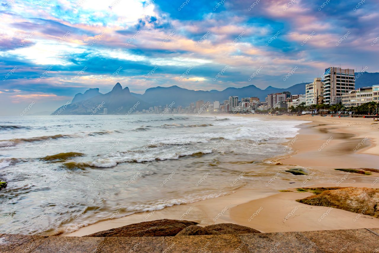Ipanema no Rio de Janeiro ao entardecer com céu nublado, montanhas ao fundo e vegetação nas laterais da praia