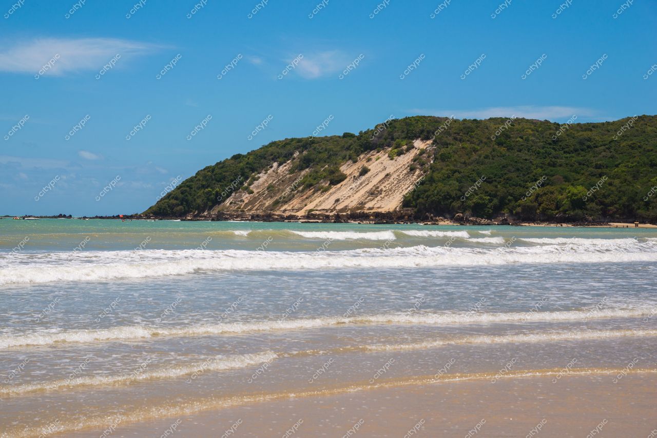 Natal, Rio Grande do Norte, praia com águas calmas e morro verdejante ao fundo em dia ensolarado