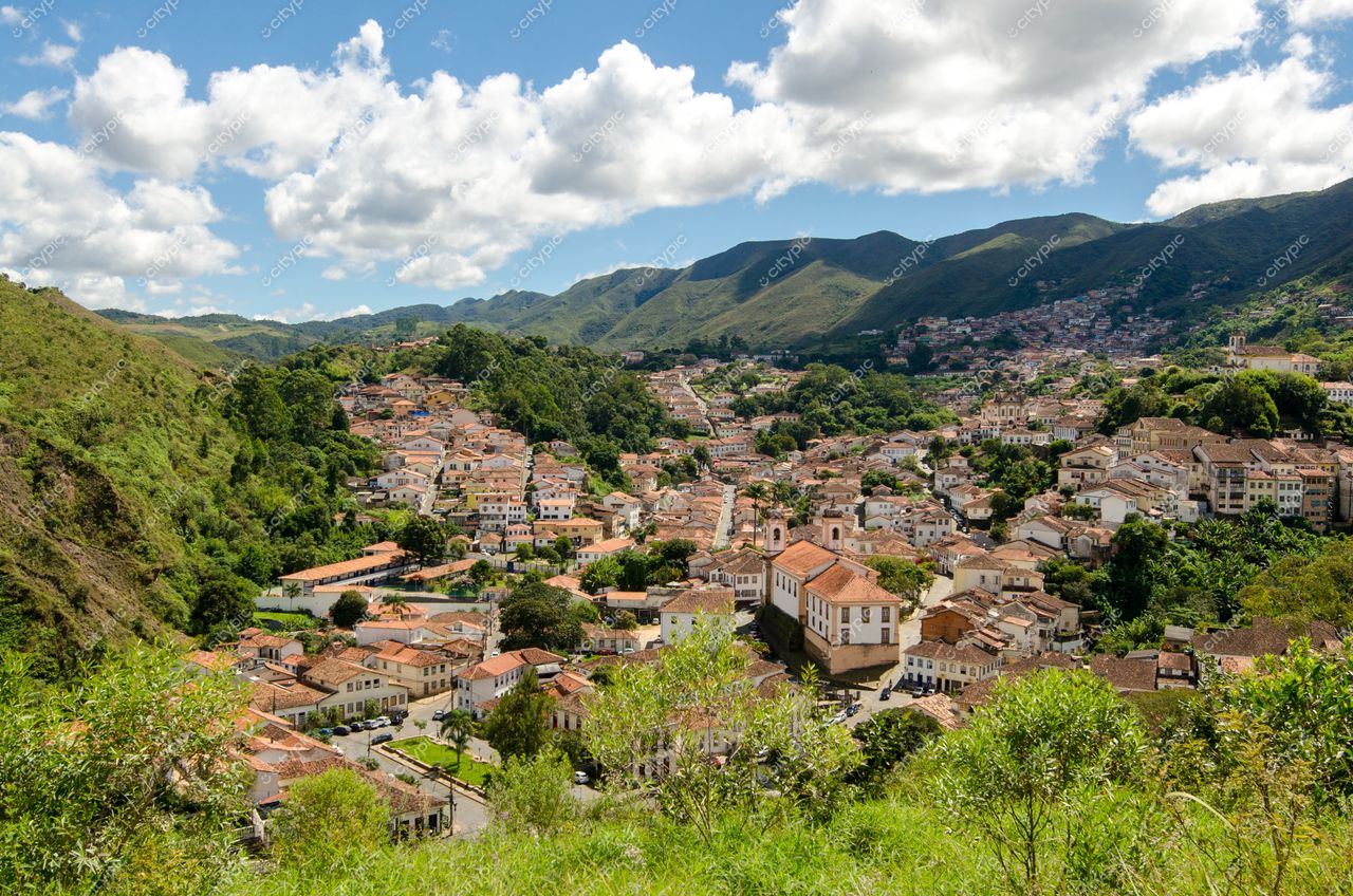 Ouro Preto, Minas Gerais em dia ensolarado com arquitetura colonial e vegetação abundante entre ruas sinuosas e montanhas