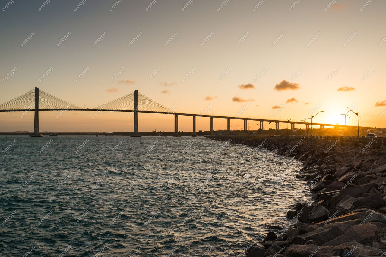 Natal, Rio Grande do Norte, pôr do sol sobre o viaduto com tráfego e rochas à beira-mar