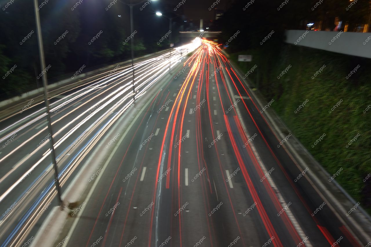 São Paulo, São Paulo, via expressa à noite com tráfego intenso e vegetação densa ao longo das faixas iluminadas