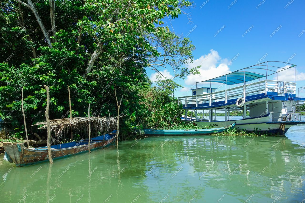 Brejo Grande, Sergipe, canoa de madeira e barco moderno em canal tranquilo com vegetação densa e céu claro