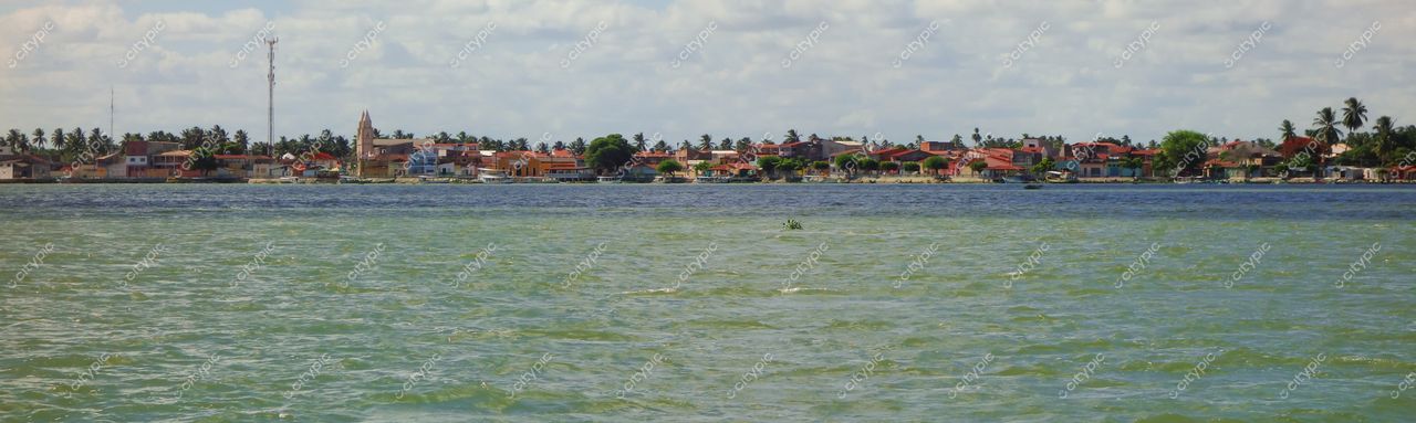 Brejo Grande, Sergipe com casas coloridas à beira-mar e vegetação nas margens sob céu parcialmente nublado