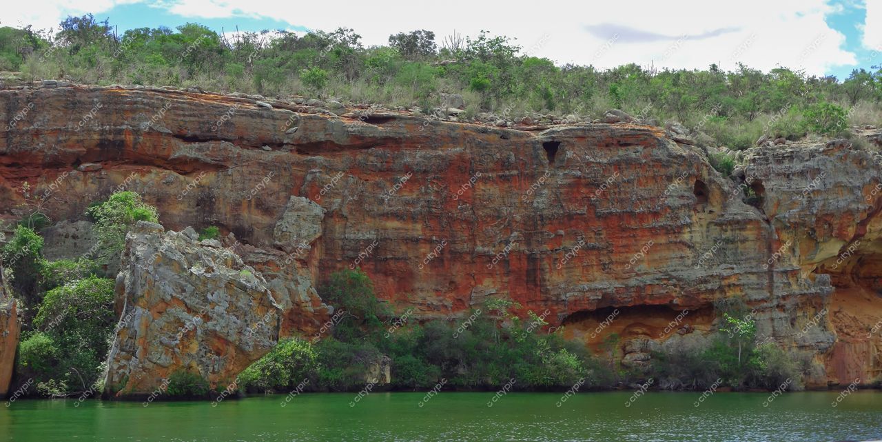 Canindé de São Francisco, Sergipe com formação rochosa avermelhada à margem de lago em dia ensolarado e vegetação abundante