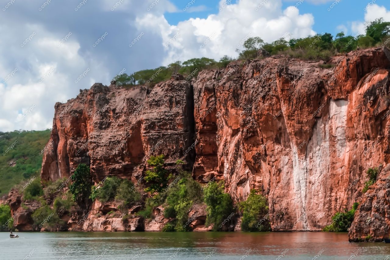 Canindé de São Francisco, Sergipe, formação rochosa avermelhada com vegetação verde e lago refletindo luz suave do dia