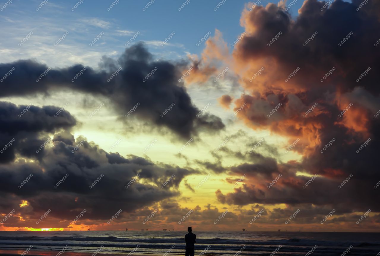 Aracaju, Sergipe, silhueta de homem na areia da praia durante pôr do sol com céu laranja e nuvens escuras
