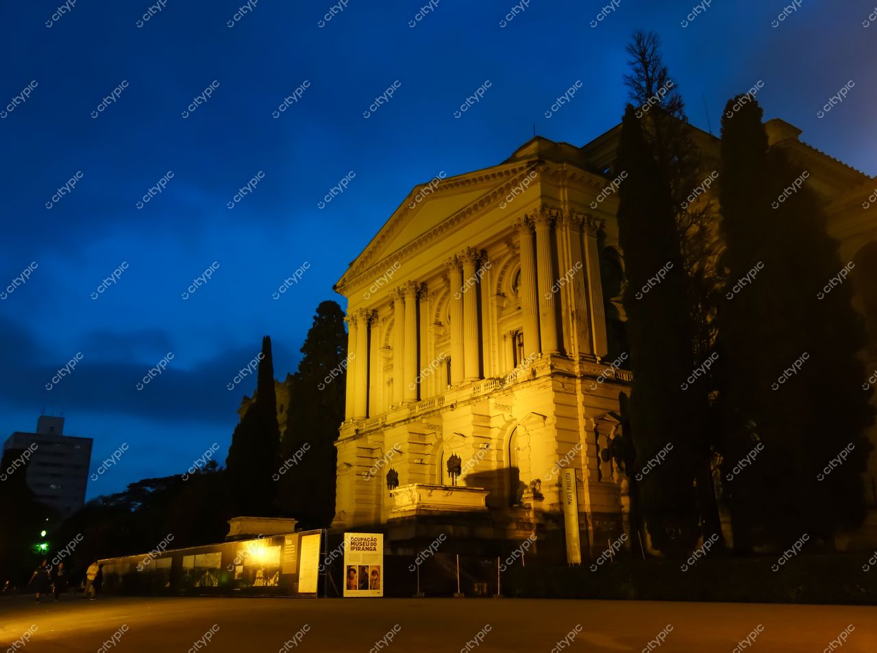 São Paulo, São Paulo, fachada de edifício histórico neoclássico iluminada ao crepúsculo com árvores e pessoas na calçada