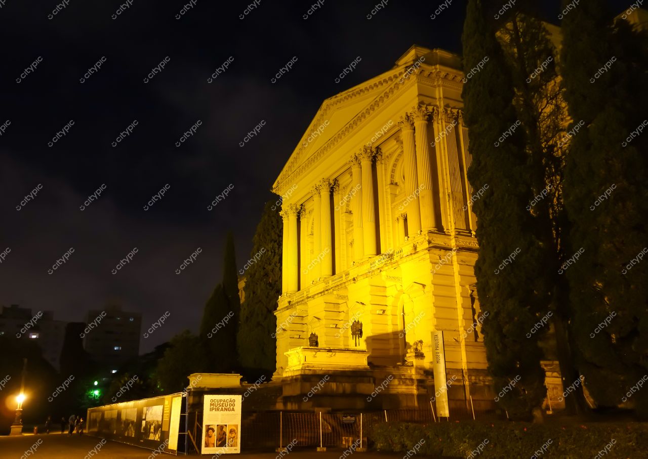São Paulo, São Paulo, fachada iluminada de edifício histórico à noite com árvores e céu nublado ao fundo