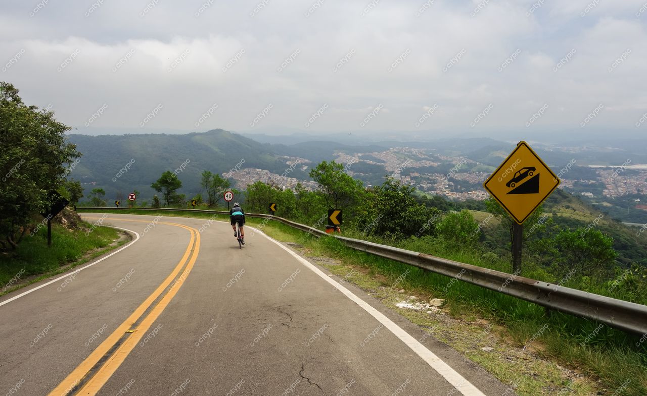 São Paulo, São Paulo, ciclista em estrada sinuosa com montanhas ao fundo e vegetação verdejante nas margens
