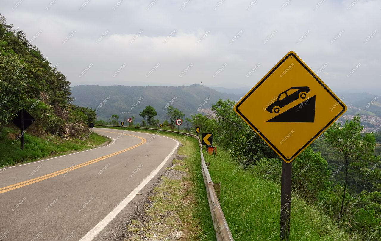 São Paulo, São Paulo, estrada sinuosa em área montanhosa com sinal de advertência e vegetação verdejante ao redor