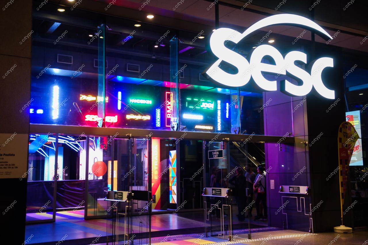 Avenida Paulista em São Paulo com fachada do Sesc iluminada por neon e movimento de pessoas à noite