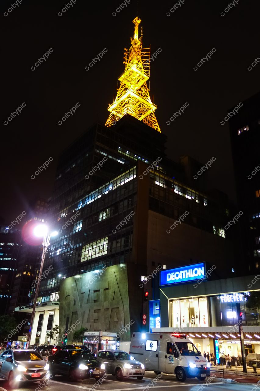 Avenida Paulista em São Paulo à noite com o edifício da Gazeta iluminado e tráfego intenso de veículos