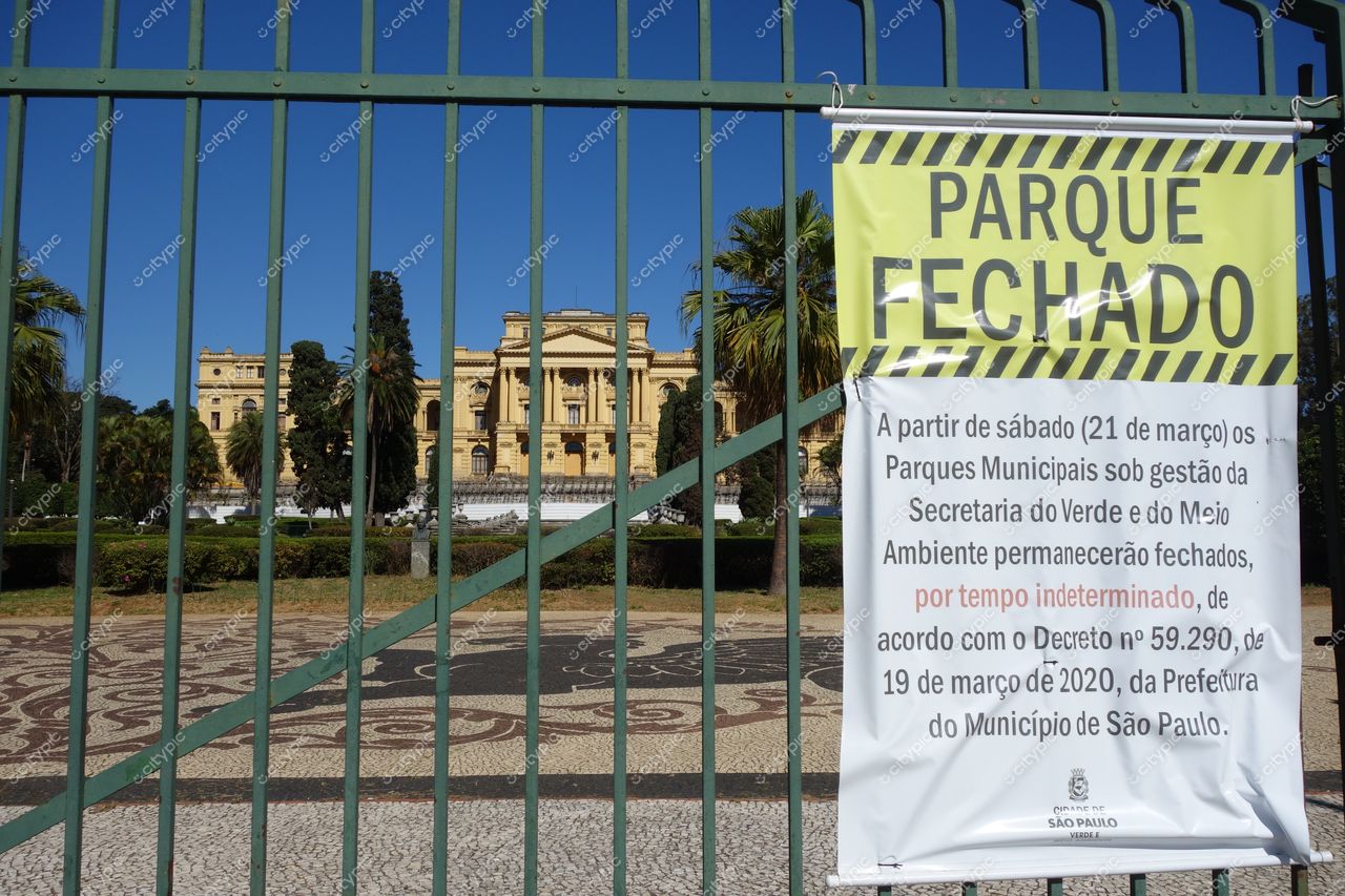São Paulo, São Paulo, entrada de parque fechado com grade verde e aviso, edifício amarelo ao fundo e palmeiras