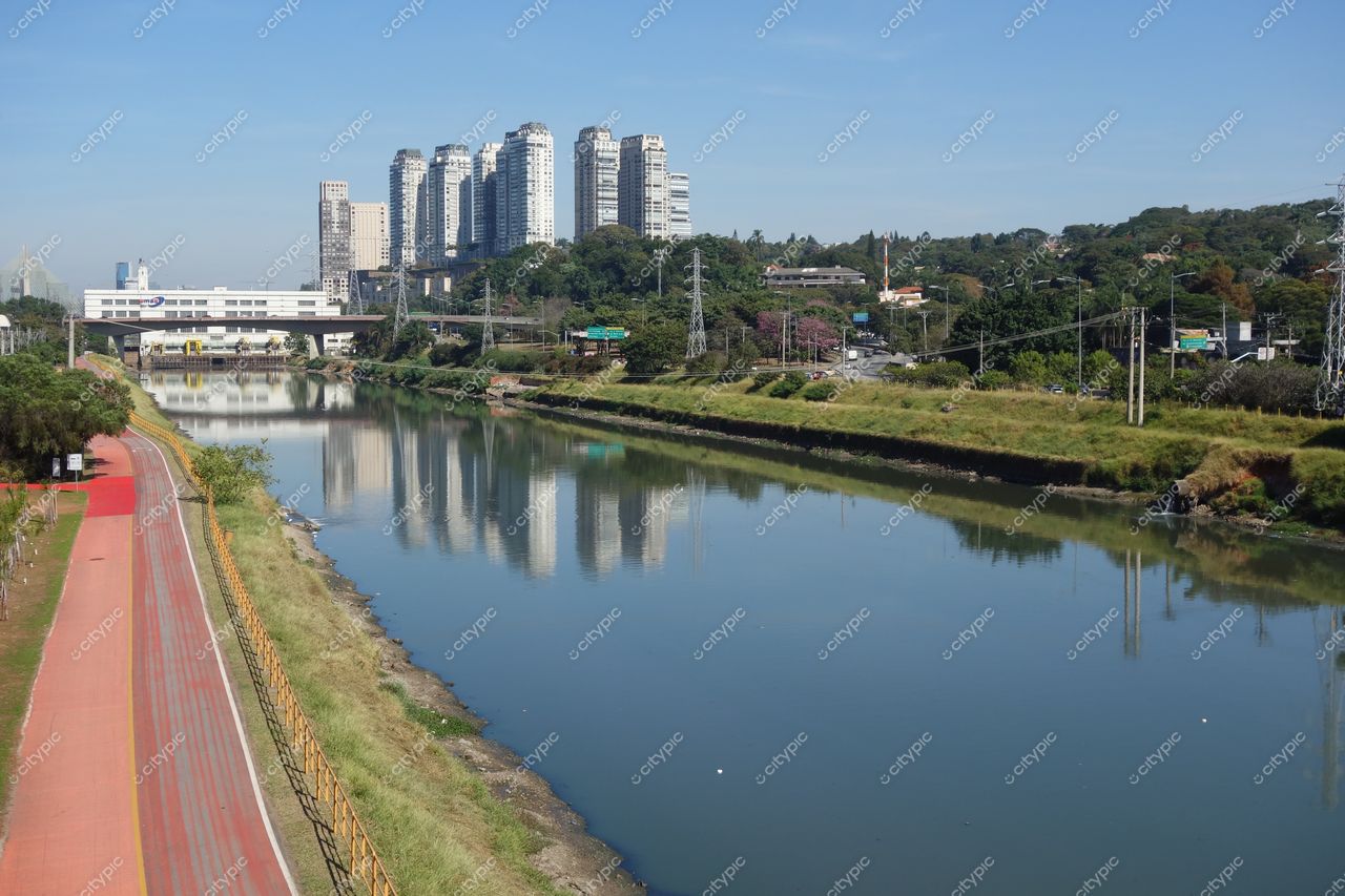 São Paulo, São Paulo, vista do rio refletindo edifícios com ciclofaixa vermelha e vegetação sob céu ensolarado