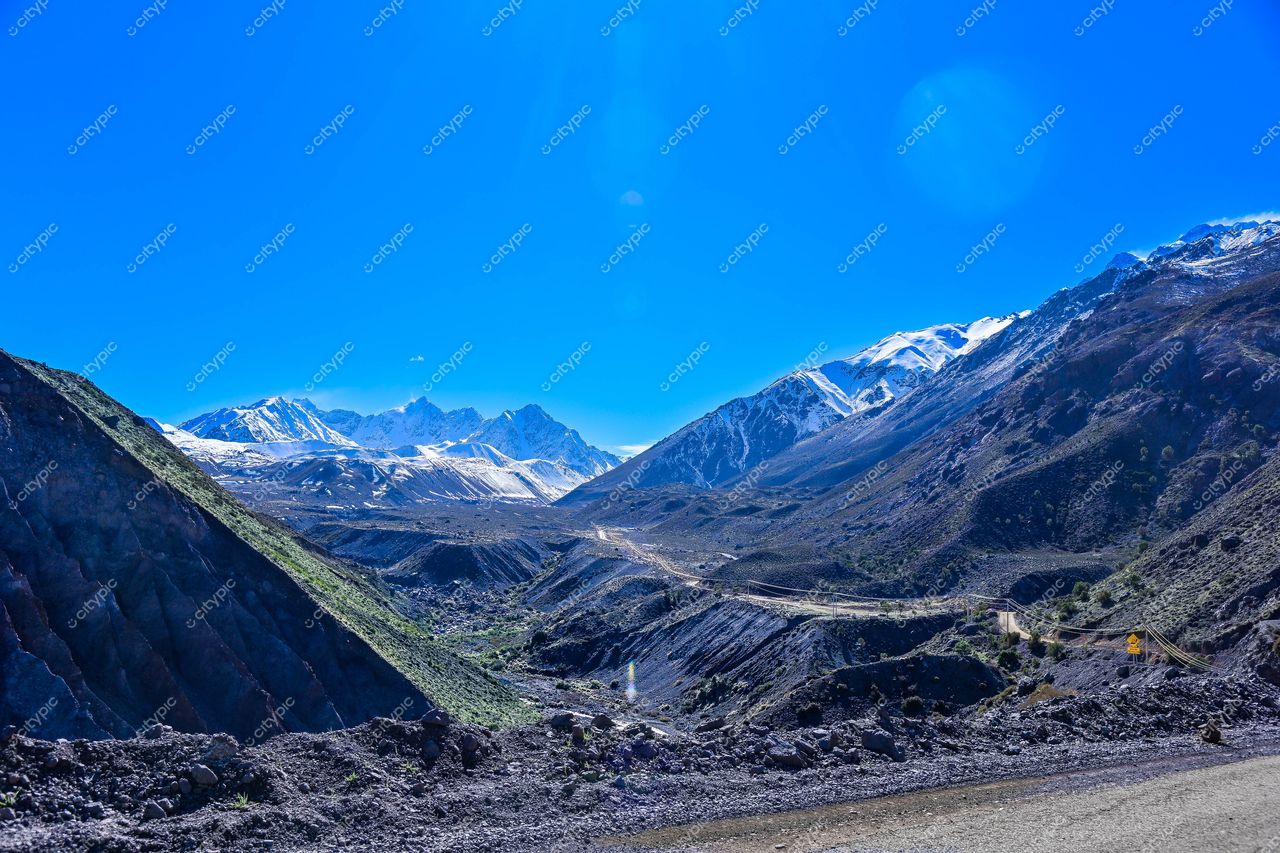 Paisagem montanhosa com céu azul e estrada sinuosa, destacando relevo e vegetação esparsa sob luz solar