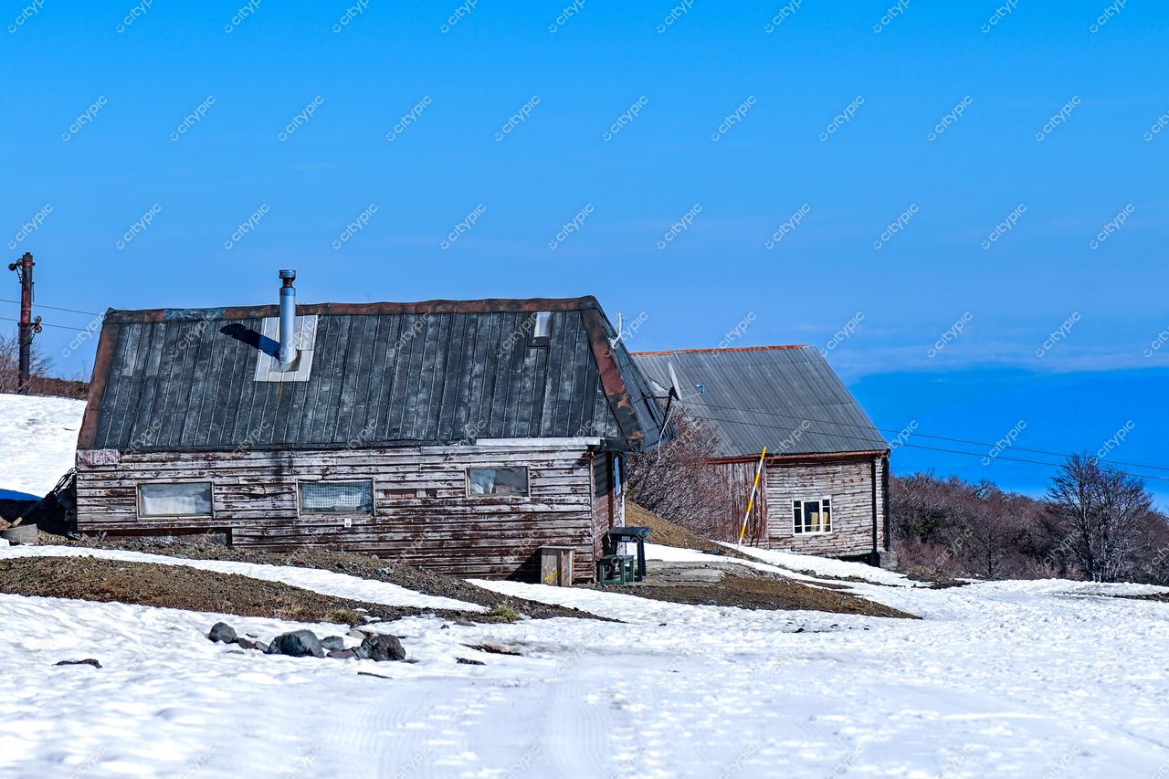 Casas de madeira com telhados metálicos em área coberta de neve sob céu azul em ambiente rural montanhoso