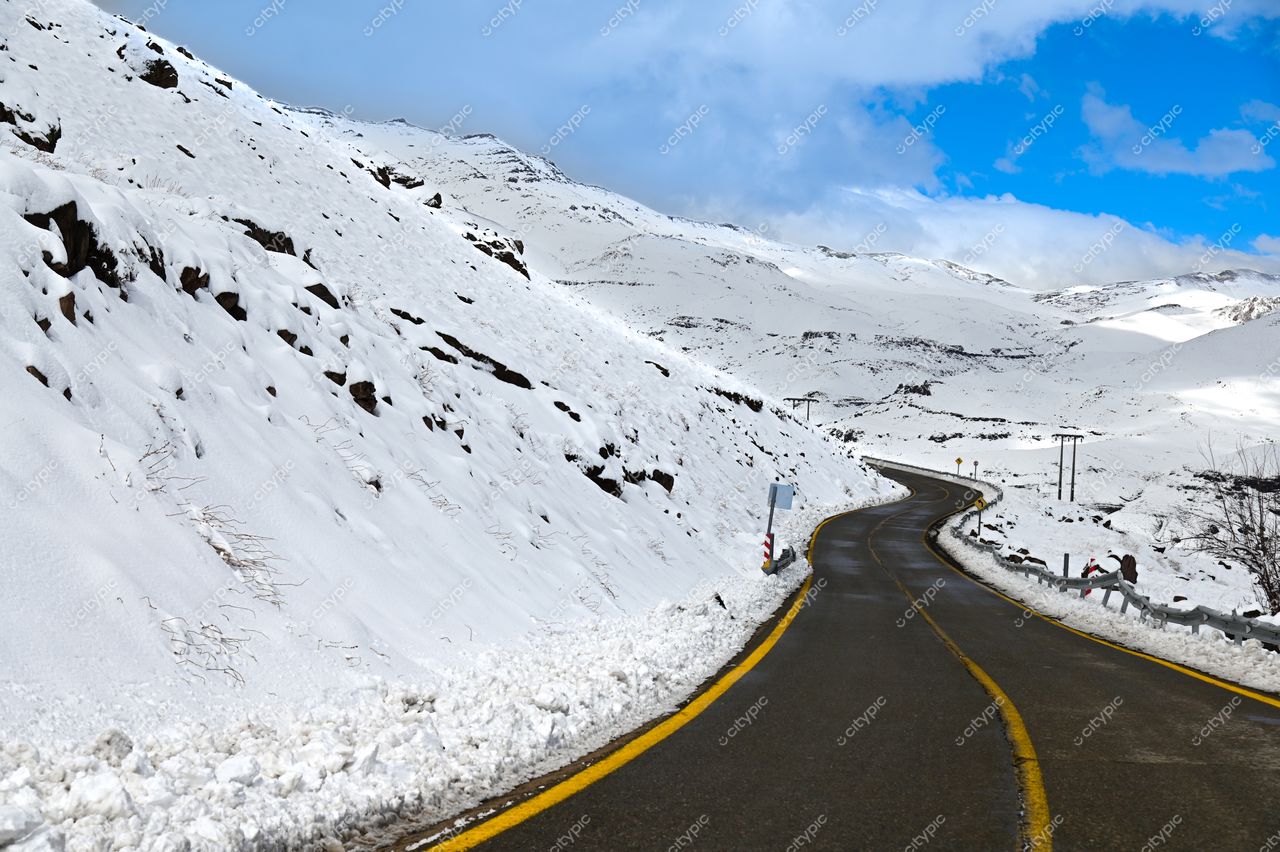 Estrada sinuosa coberta de neve com montanhas ao fundo e céu parcialmente nublado em ambiente invernal