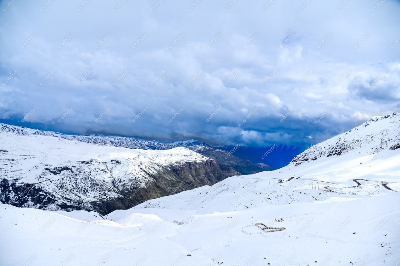 Paisagem montanhosa nevada com céu nublado e estradas sinuosas, capturada em iluminação suave durante o dia