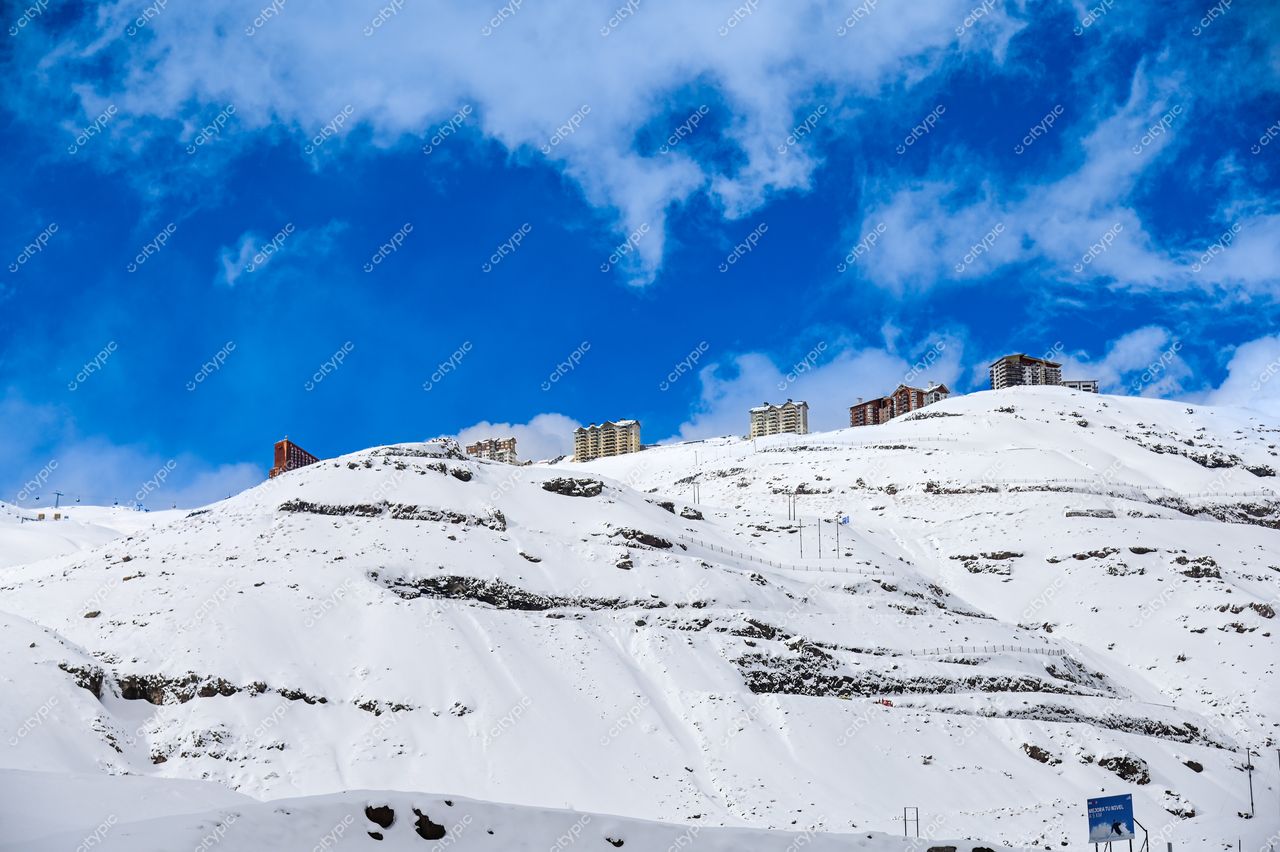 Paisagem montanhosa coberta de neve com edifícios claros sob céu azul e nuvens brancas em dia tranquilo