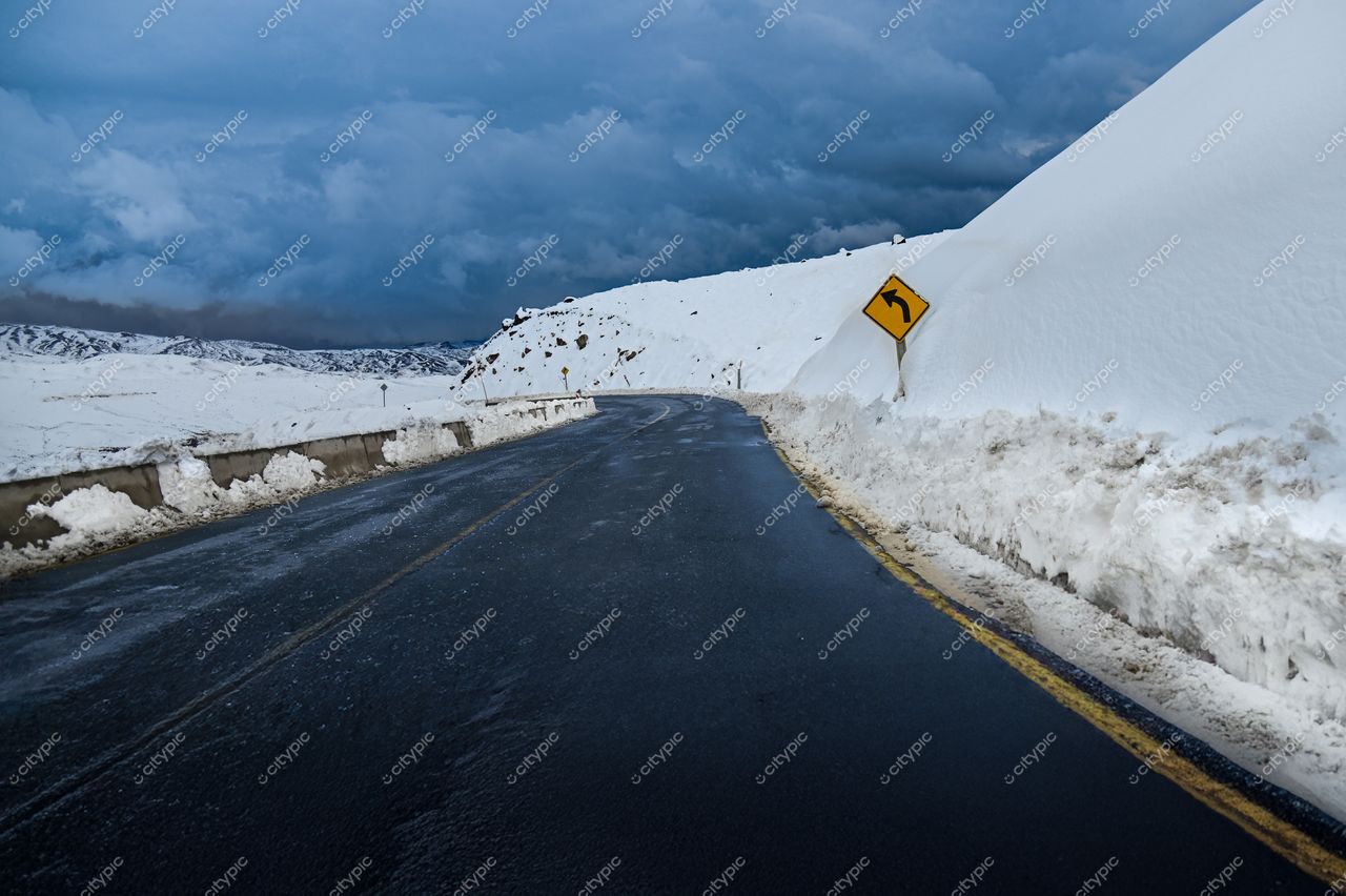 Estrada pavimentada em paisagem nevada com céu nublado e sinal de curva à direita em ambiente isolado