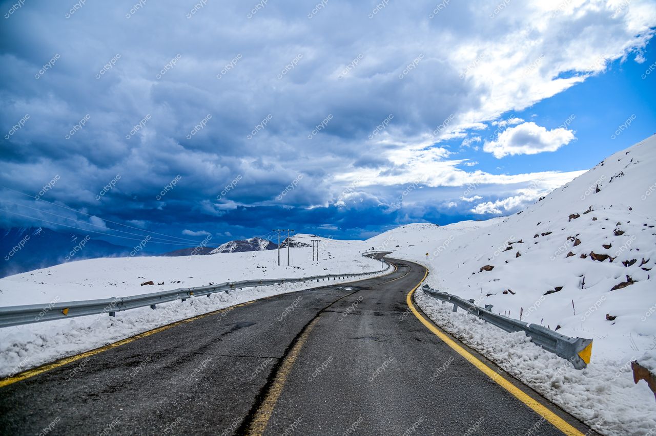 Estrada sinuosa coberta de neve com montanhas ao fundo sob céu nublado e iluminação natural fria