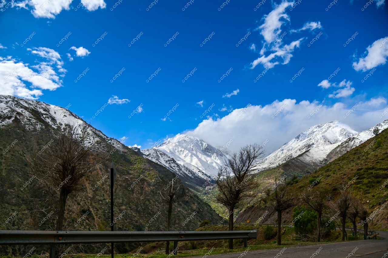 Estrada sinuosa em paisagem montanhosa com picos nevados e céu azul em dia ensolarado e claro