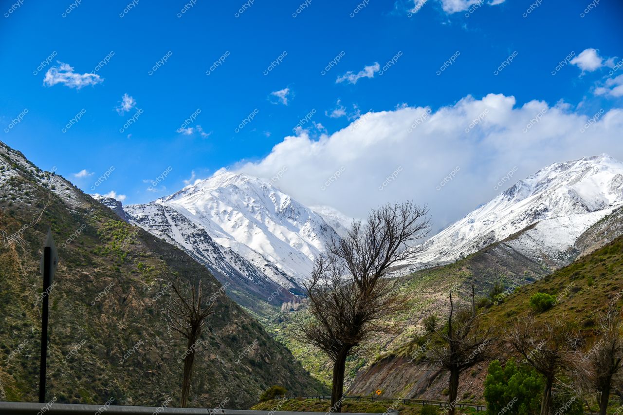 Paisagem montanhosa com picos nevados e encostas verdes, céu azul claro e estrada acessível para exploração