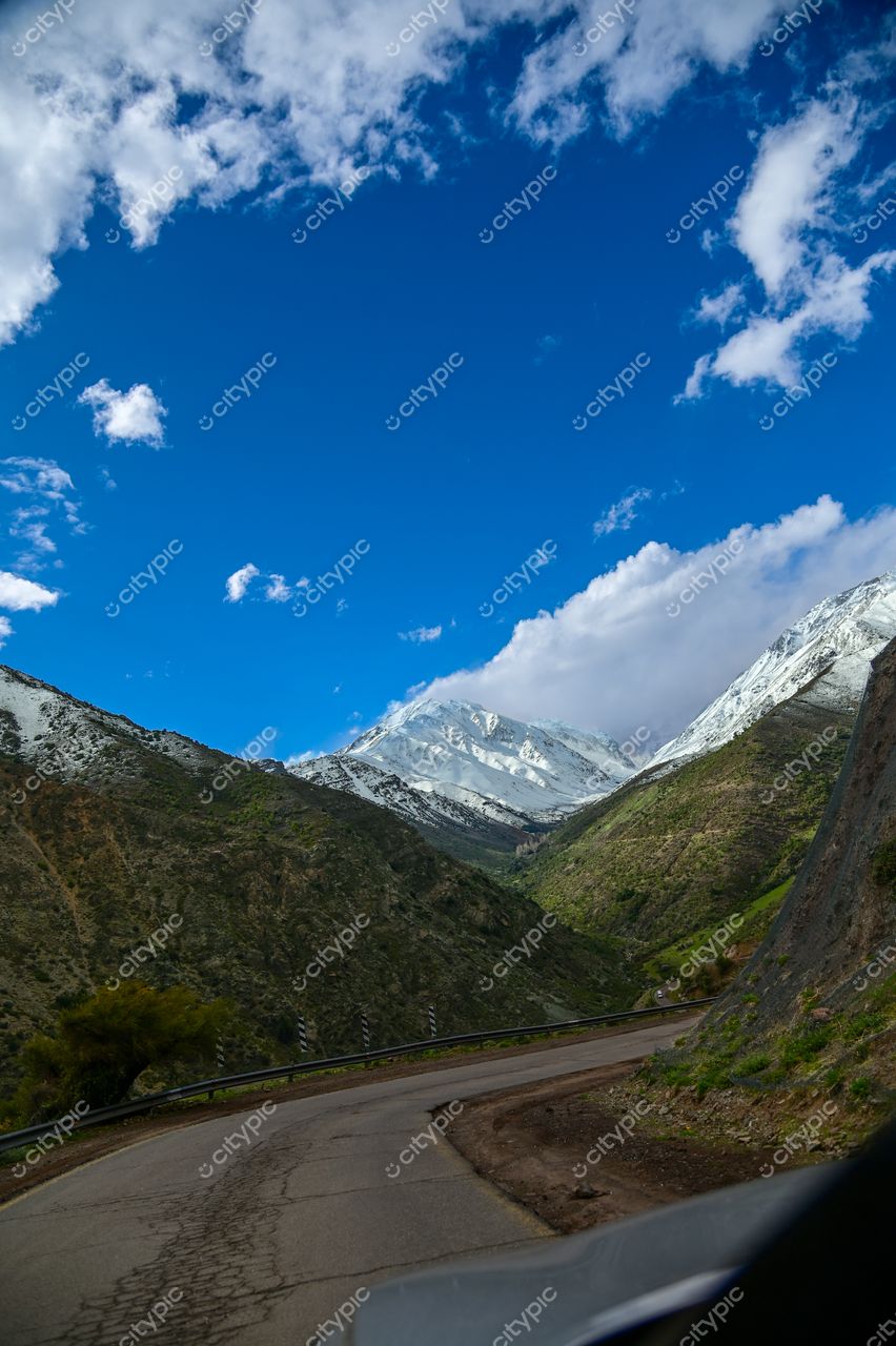 Estrada sinuosa entre montanhas nevadas com céu azul e nuvens brancas em dia claro de primavera ou outono