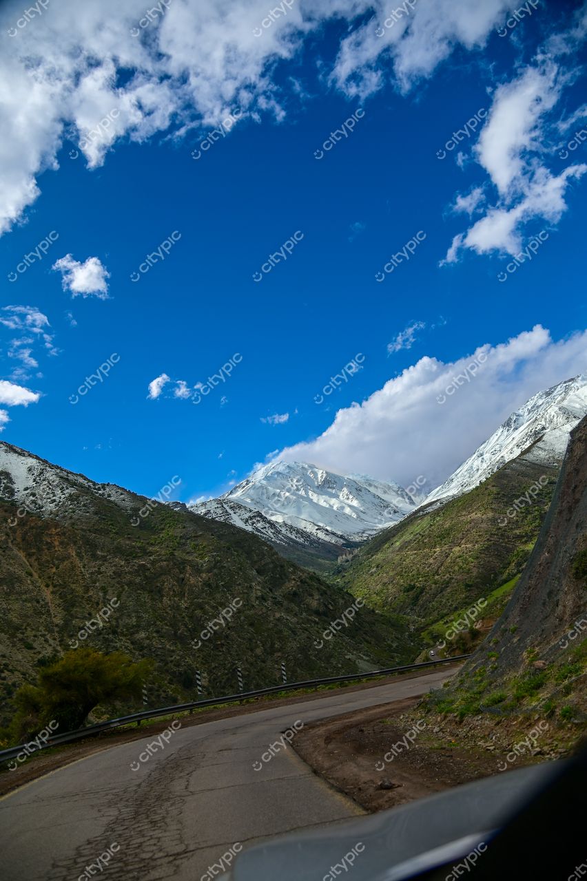 Estrada sinuosa em paisagem montanhosa com vegetação verde e montanha nevada sob céu azul claro