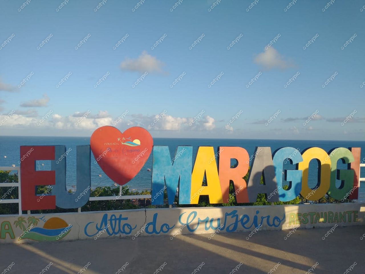 Maragogi, Alagoas com a frase EU ♥ MARAGOGI em letras coloridas e céu claro ao fundo durante o dia