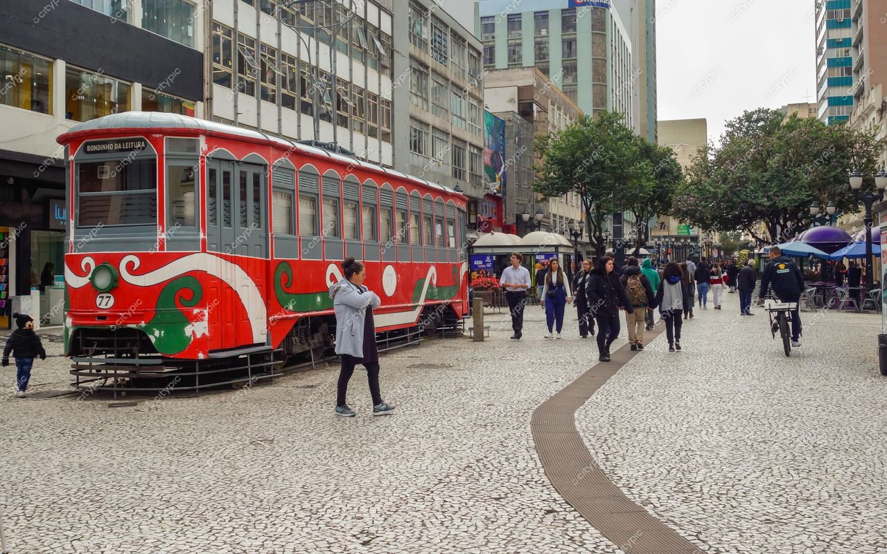 Rua XV de Novembro em Curitiba com bonde vermelho entre pedestres e prédios modernos em dia nublado