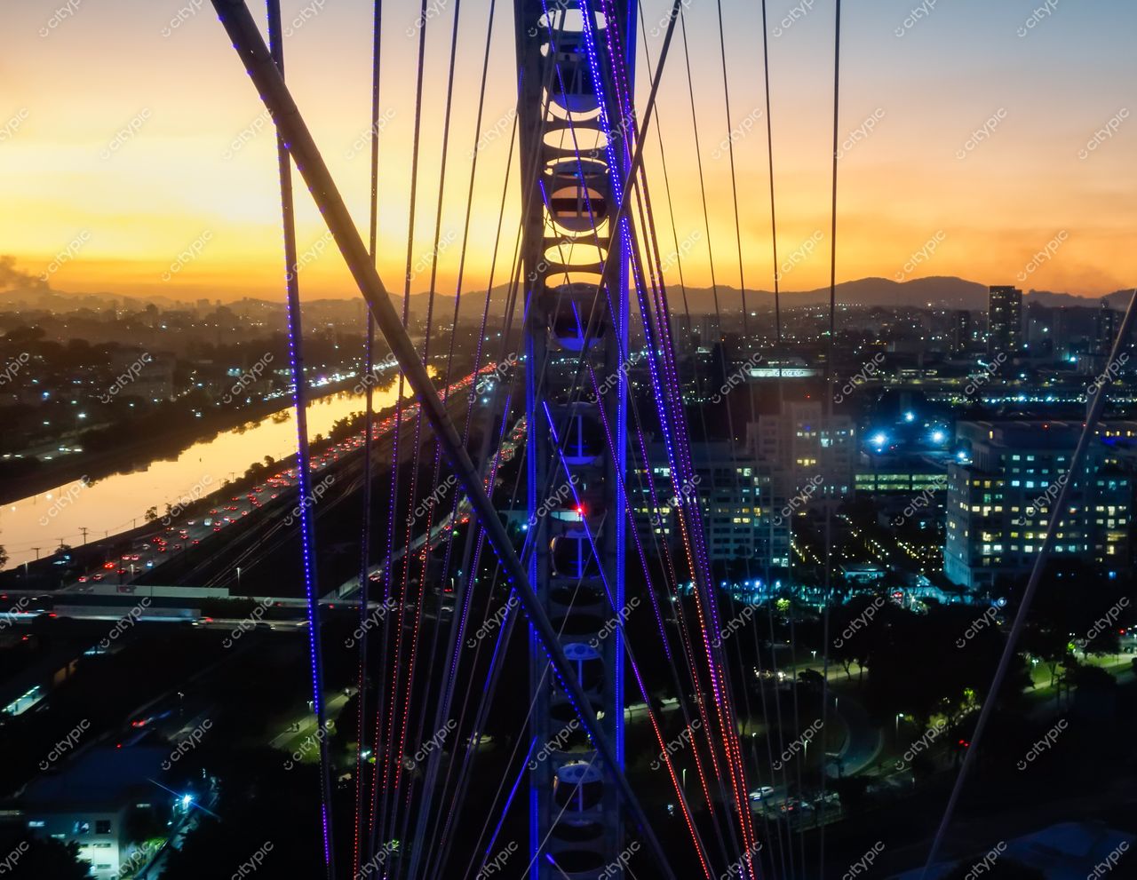 São Paulo, São Paulo, vista noturna com roda-gigante iluminada e pôr do sol alaranjado ao fundo