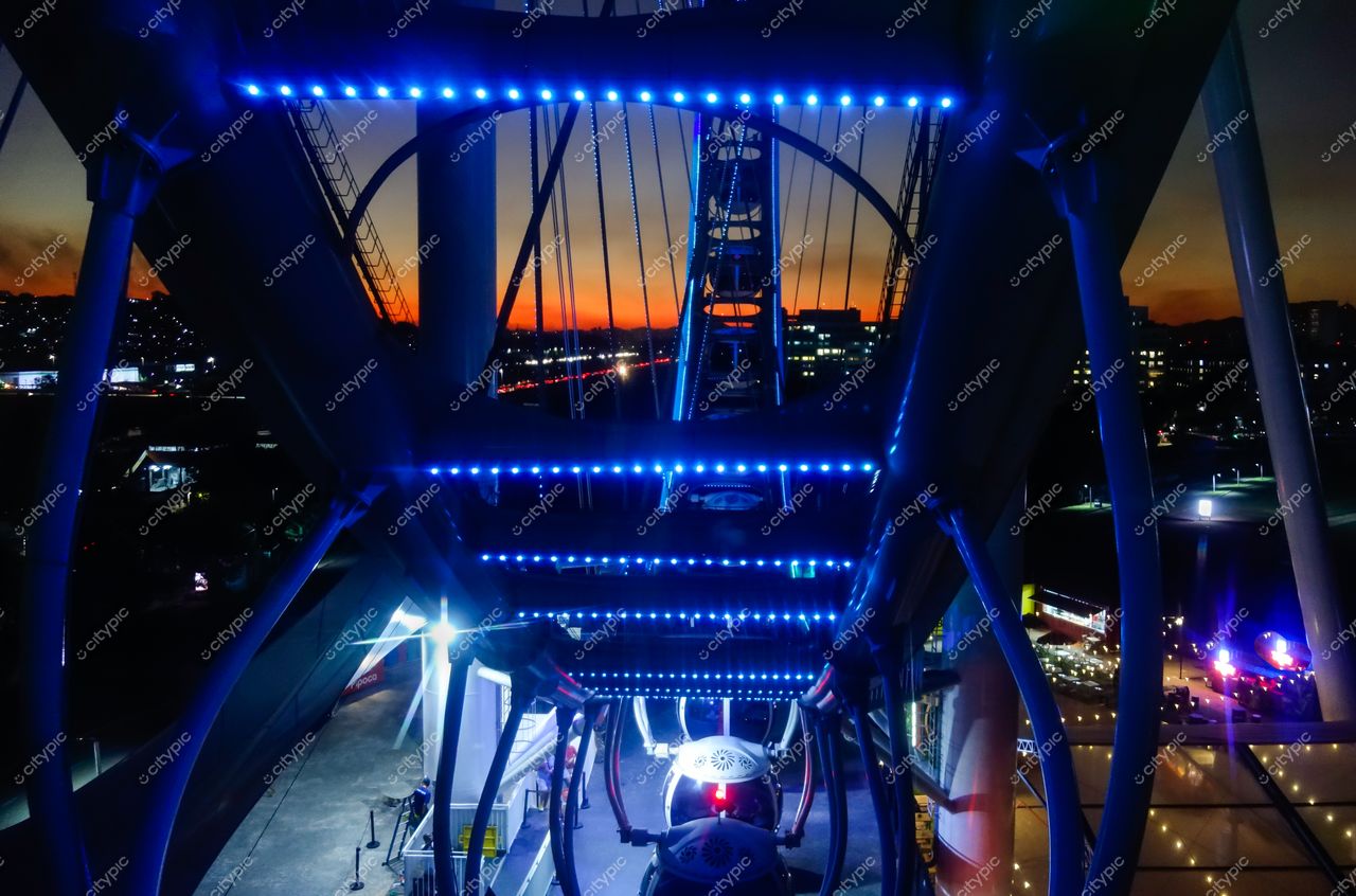 São Paulo, São Paulo, vista noturna da roda-gigante iluminada em azul com pôr do sol alaranjado ao fundo