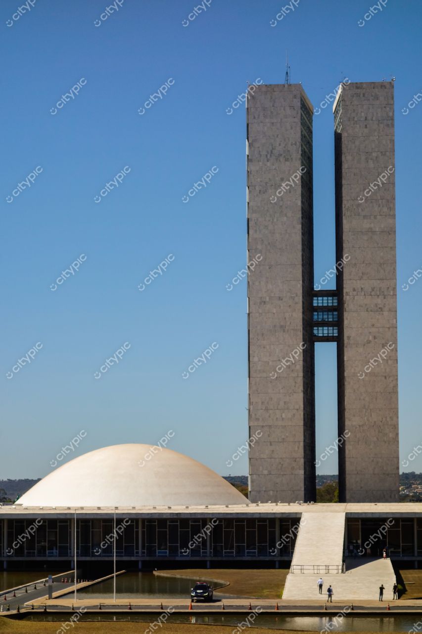 Congresso Nacional em Brasília com céu azul, iluminação clara, pedestres e vegetação ao redor da arquitetura moderna
