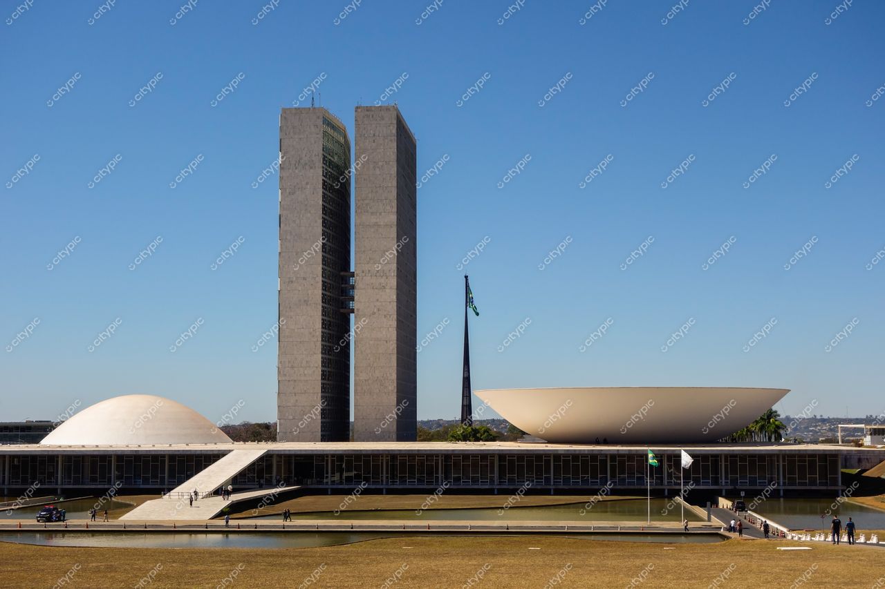 Congresso Nacional em Brasília sob céu azul claro com cúpulas visíveis e pessoas caminhando em área gramada