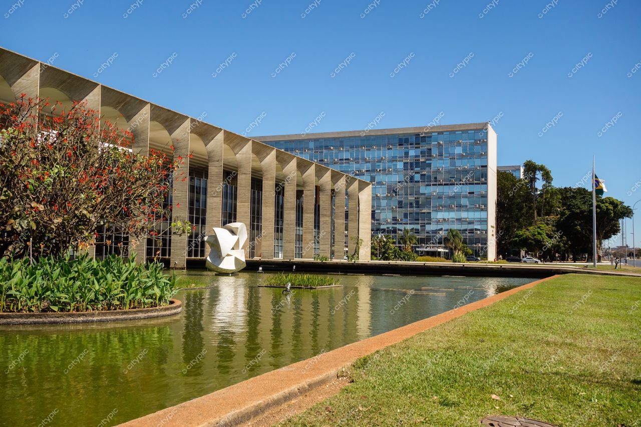 Palácio do Itamaraty em Brasília com lago sereno, vegetação ao redor e escultura contemporânea sob luz solar