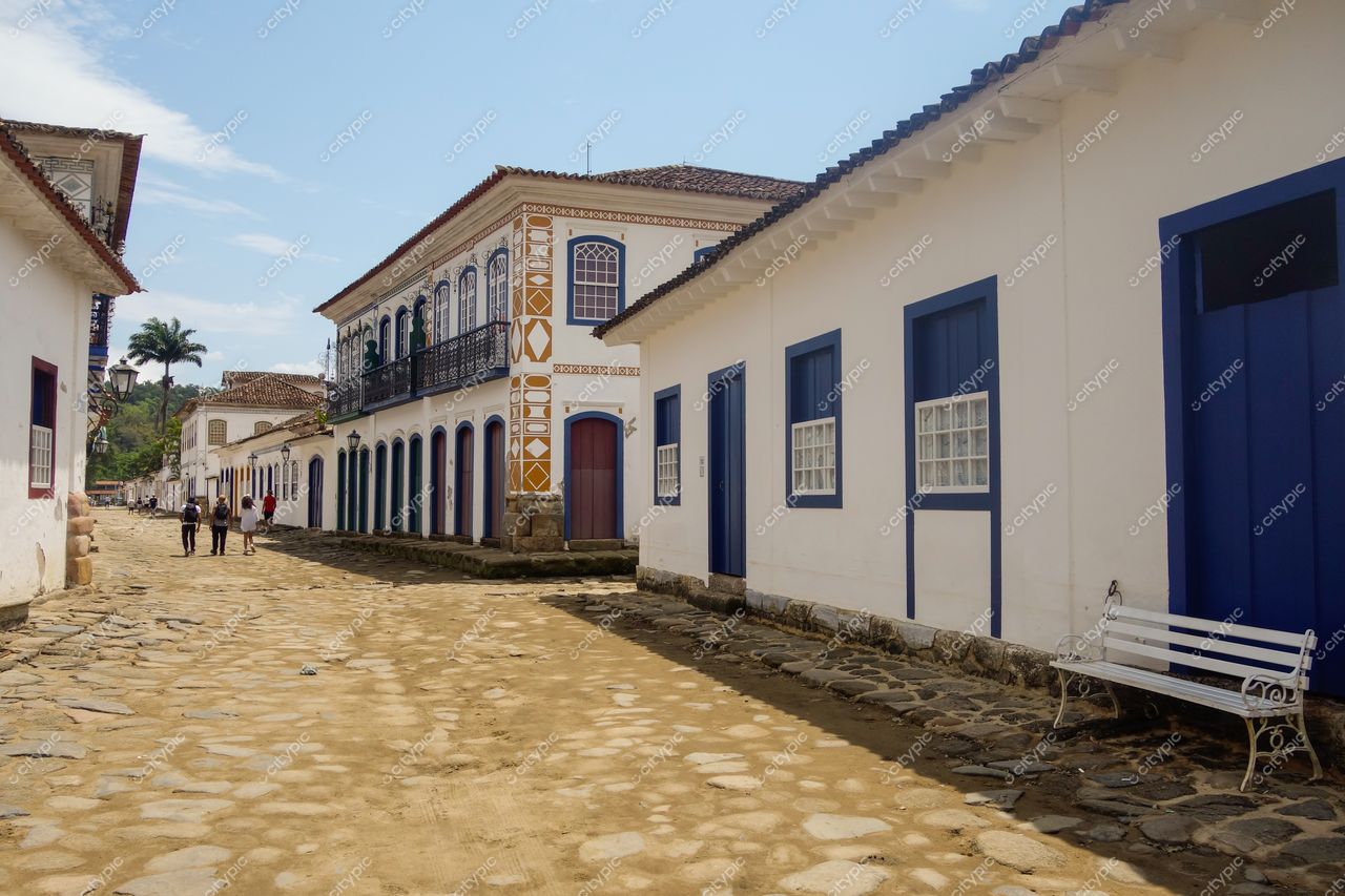 Paraty, Rio de Janeiro, rua tranquila com calçamento em pedras e casas brancas com detalhes azuis sob luz solar